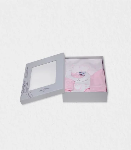 Flat-lay of the ivory-and-blush baby gift set—pyjama, blanket and hat—displayed beside Dubai skyline postcard and date-palm fronds, illustrating organic cotton softness and heart embroidery for parents seeking a Dubai baby gift shipped worldwide with eco-friendly credentials and fast delivery.
